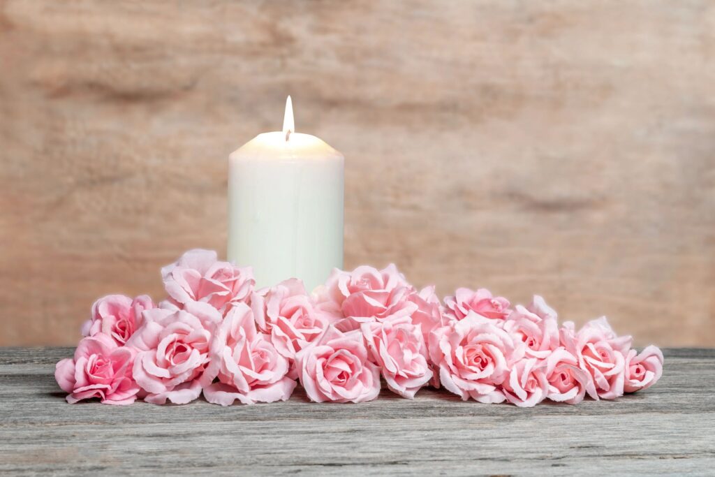 Burning candle and elegant pink roses arrangement on wooden background.