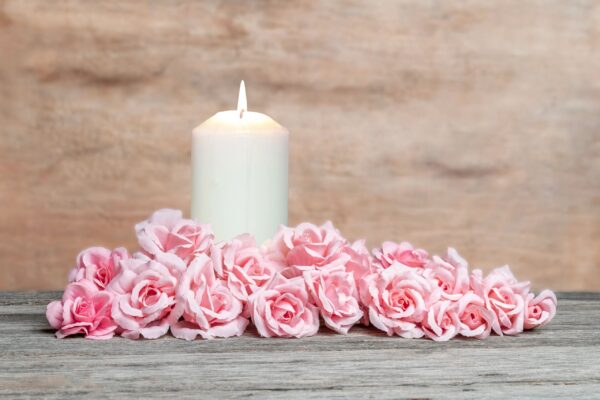 Burning candle and elegant pink roses arrangement on wooden background.
