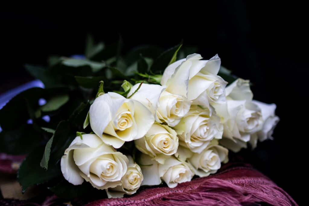 Elegant bouquet of white roses on a soft woven cloth against a dark background captured in moody light symbolizing purity remembrance and romance with fresh greenery accents