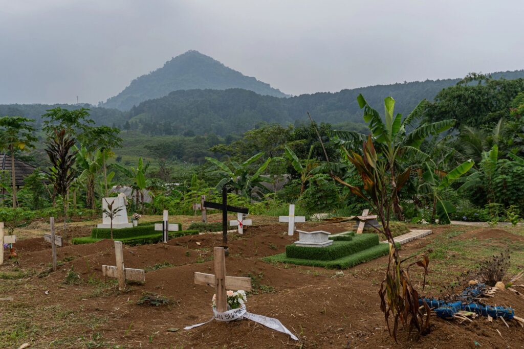 A rural Christian cemetery located in a green hillside setting with wooden and stone cross markers, some decorated with flowers.